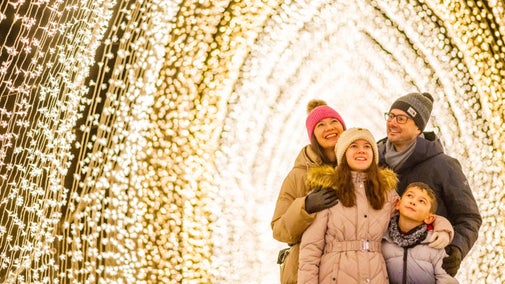 Two adults and two children stand in a cathedral-like archway of bright lights.